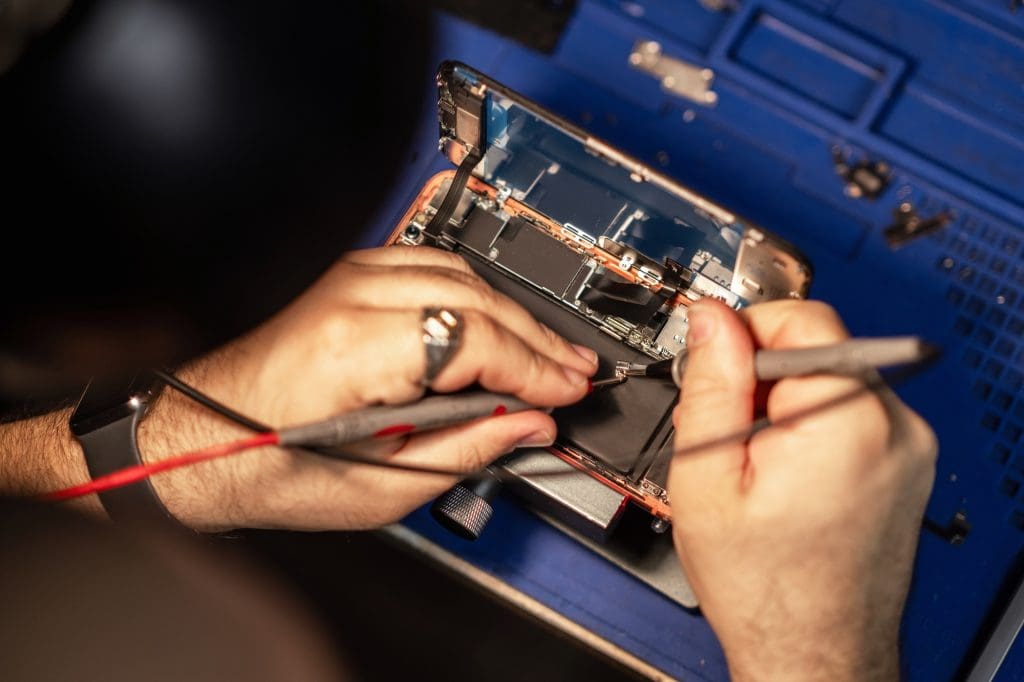 Technician performing smartphone battery repair with specialized tools on a workbench in a well-lit